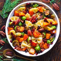 a bowl filled with pasta and vegetables on top of a wooden table next to pecans