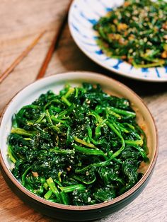 two bowls filled with green vegetables on top of a wooden table