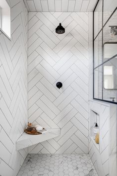 a walk in shower sitting next to a white tiled wall and floor with black fixtures