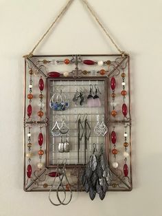 a metal frame with earrings and earring hooks hanging on a wall next to a pair of scissors