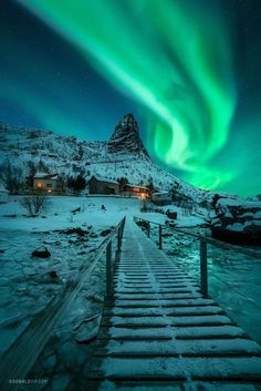 the aurora bore is lit up in the sky above a snow covered mountain and wooden walkway