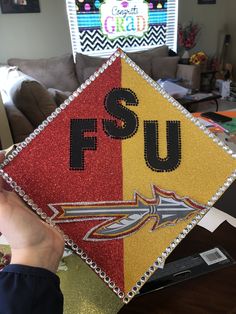 someone holding up a graduation cap with the word fsu on it in front of a couch