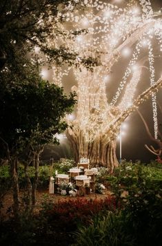 a large tree with lights hanging from it's branches in the middle of a garden