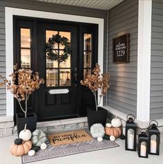 front porch decorated for fall with pumpkins, candles and wreath on the door mat