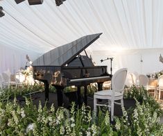 a grand piano is surrounded by flowers and greenery in front of a white tent