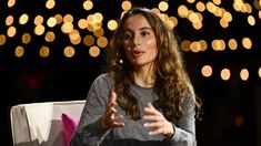 a woman sitting in front of a table with her hands out and lights behind her