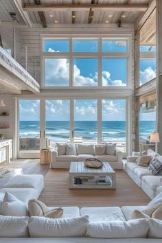 a living room filled with lots of white furniture and windows overlooking the beach in front of it