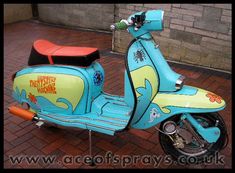 a blue scooter with an orange seat on brick pavement in front of a building