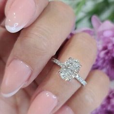 a woman's hand holding a ring with a flower on it and pink flowers in the background