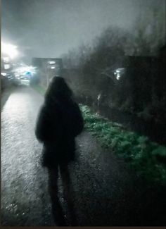 a person walking down a street at night in the rain with an umbrella over their head