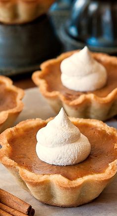 mini pumpkin pies with whipped cream on top and cinnamon sticks in the foreground