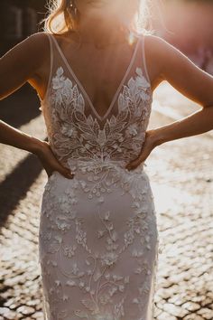 a woman in a white wedding dress standing on a cobblestone street with her back to the camera