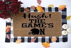 a door mat that says hush the game's on with fall leaves and pumpkins around it