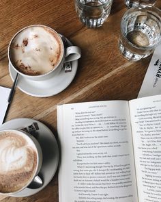 an open book sitting on top of a wooden table next to two cups of coffee