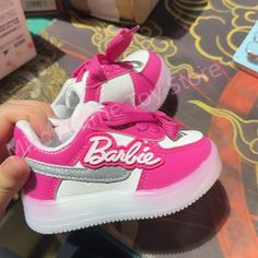 a hand holding a pink and white shoe with the word barbie on it's side