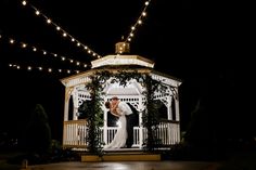 a bride and groom standing in front of a gazebo lit up with fairy lights