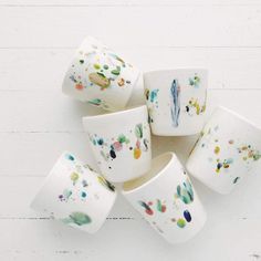 five white cups with colorful paint splattered on them sitting next to each other