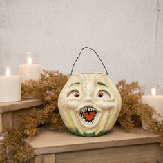 a ceramic pumpkin with a creepy face on it's head and some candles around it