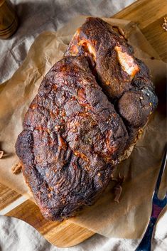 a large piece of meat sitting on top of a wooden cutting board next to a knife and fork