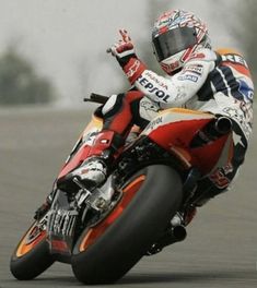 a man riding on the back of a motorcycle down a race track with his hand in the air