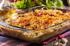 a casserole dish filled with pasta and vegetables on a table next to olive oil