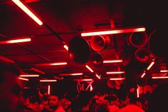 a group of people in a dark room with red lights and speakers hanging from the ceiling