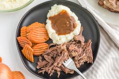 a black plate topped with meat, mashed potatoes and carrots