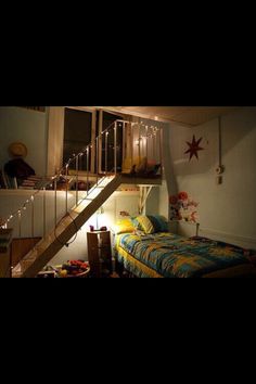 a bed sitting under a stair case next to a wall with lights hanging from it