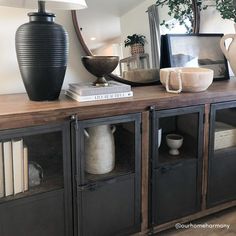 a black vase sitting on top of a wooden table next to a mirror and bookshelf