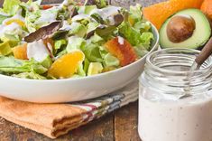 a salad with dressing and an avocado in a bowl next to it on a wooden table