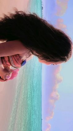 a woman with long black hair standing next to the ocean