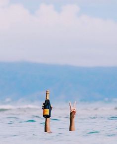 two people in the ocean holding up bottles and pointing at them with their fingers to the sky