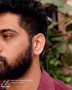 a close up of a man with a beard and piercing on his ear looking to the side