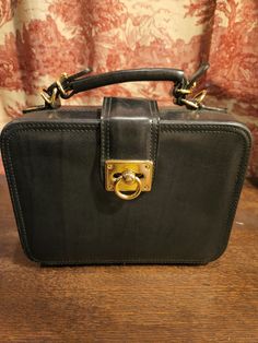 A Perfect Square OR close to it (8x6)! Adorable Black Leather w/Gold Trim transitional bag from the 1980s...Square shaped with a top handle and a removable shoulder strap. Flap over closure, footed bottom, and middle zipper pocket.  Compact and stylish in a vintage bag! Vintage Satchel With Detachable Strap For Business, Vintage Business Satchel With Detachable Strap, Retro Formal Satchel Briefcase, Vintage Top Handle Briefcase For Formal Use, Rectangular Formal Satchel With Brass Hardware, Retro Rectangular Business Shoulder Bag, Formal Rectangular Satchel With Brass Hardware, Formal Square Briefcase With Top Carry Handle, Retro Rectangular Business Bags