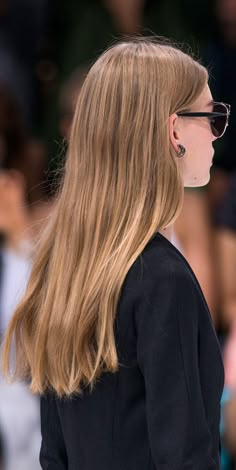 a woman with long blonde hair wearing sunglasses and a black jacket is standing in front of a crowd