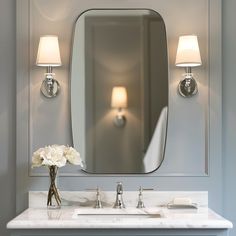 a bathroom sink with a mirror above it and two lamps on the wall behind it