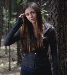 a woman standing in the woods with her hand on her head and looking off into the distance