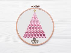 a cross stitch christmas tree is shown in pink and gold on a white wooden background