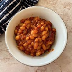 a white bowl filled with baked beans on top of a marble counter next to a black and white striped towel