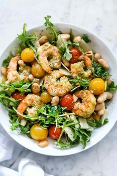 a white bowl filled with shrimp, tomatoes and lettuce on top of a marble table