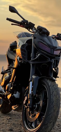 a black motorcycle parked on top of a sandy beach next to the ocean at sunset