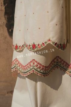 a white dress with red and green trims on it's sleeves, hanging from a hook