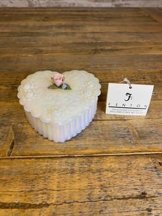 a small white heart shaped box sitting on top of a wooden table next to a tag