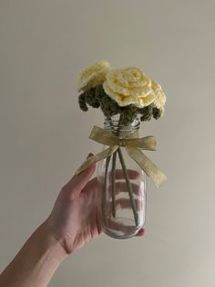 a hand holding a glass jar with flowers in it and a ribbon around the top