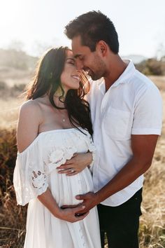 a pregnant couple cuddles and kisses in an open field