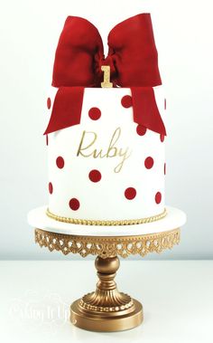 a white and red polka dot cake on a gold stand with a red bow around the top