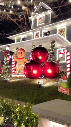 a house decorated for christmas with decorations and lights on the front yard, including large red baubies