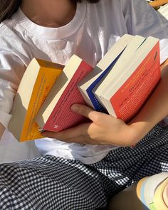 a woman is holding three books in her hands while sitting on the ground with other books