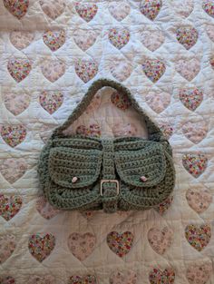 a crocheted purse laying on top of a quilted bed with hearts in the background