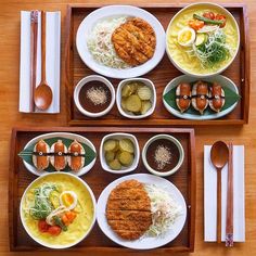 two trays filled with different types of food on top of a wooden table next to utensils